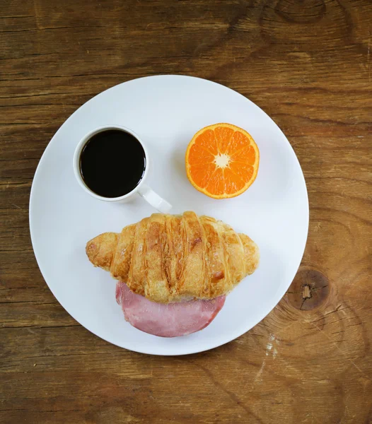 Breakfast serving funny face on the plate (croissant with ham, orange and coffee) — Stock Photo, Image