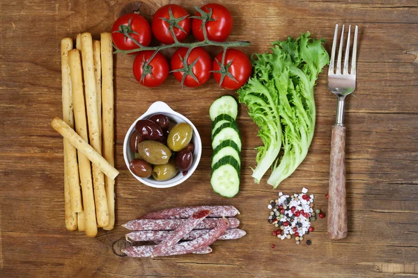 Gezond eten concept voedsel set - worstjes, brood stokken, tomaten, komkommers, sla, olijven, bovenaanzicht — Stockfoto