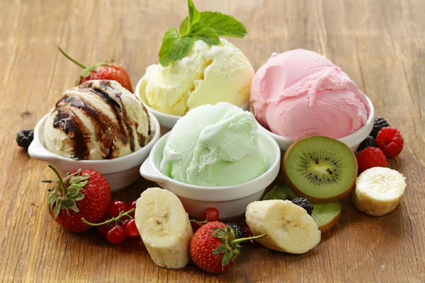 Verschiedenes Eis (Erdbeere, Banane, Minze, Schokolade) und frische Beeren auf dem Holztisch — Stockfoto