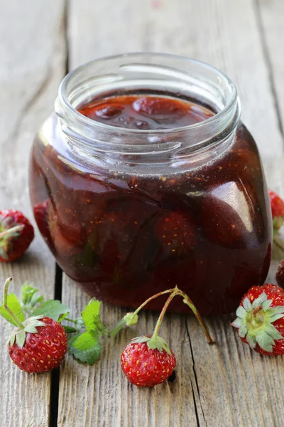 Strawberry jam in a glass jar on a wooden table, rustic style — Stock Photo, Image