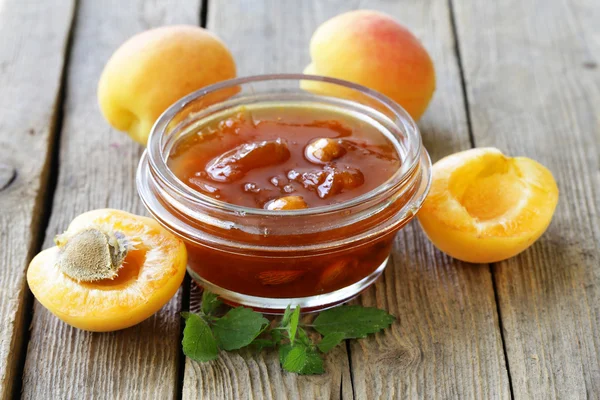 Marmellata di pesche di albicocca in un barattolo di vetro su uno sfondo di legno — Foto Stock