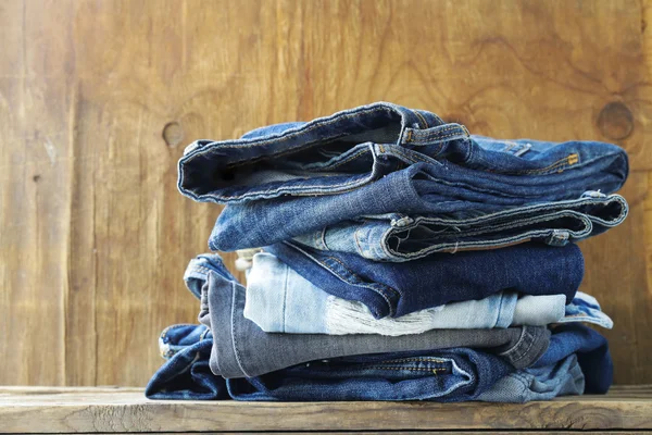 Stack of various jeans on old wooden background — Stock Photo, Image