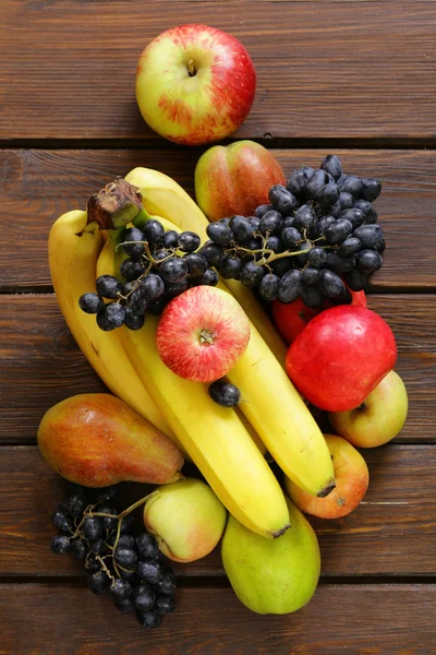 Frutas diversas (manzanas, peras, plátanos, uvas) sobre un fondo de madera — Foto de Stock