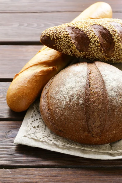 Hausgemachtes frisches Brot (Roggen, Sesam, Weiß) auf Holzgrund — Stockfoto