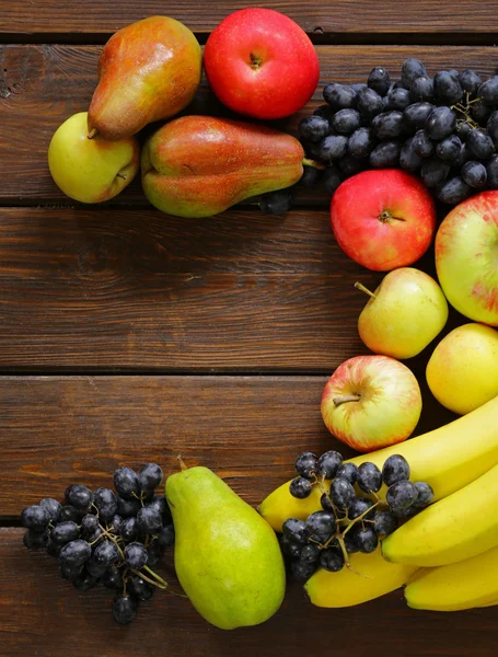 Різні фрукти (яблука, груші, банани, виноград) на дерев'яному фоні — стокове фото