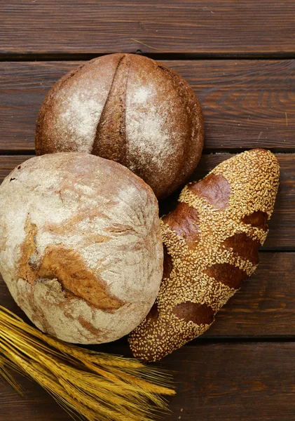 Hausgemachtes frisches Brot (Roggen, Sesam, Weiß) auf Holzgrund — Stockfoto