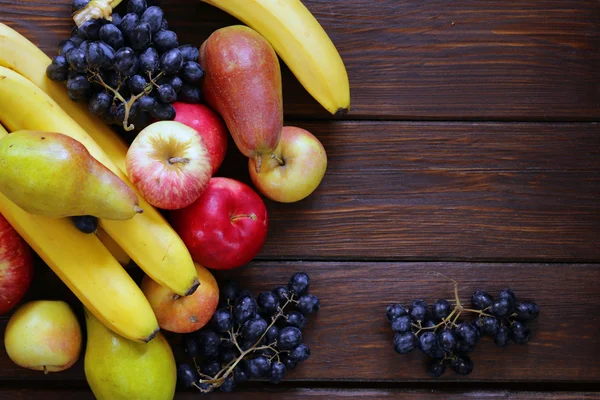 Various fruits (apples, pears, bananas, grapes) on a wooden background — Stock Photo, Image