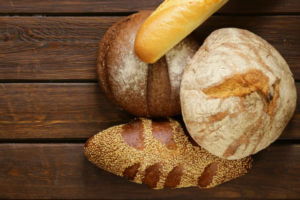 Hausgemachtes frisches Brot (Roggen, Sesam, Weiß) auf Holzgrund — Stockfoto