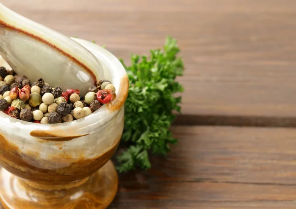 Pfefferkörner im Steinmörser auf einem Holztisch — Stockfoto