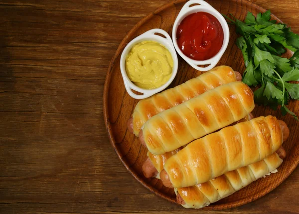 Sausage baked in dough with ketchup and mustard — Stock Photo, Image