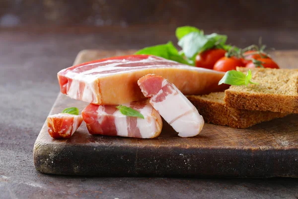 Smoked bacon with basil and tomatoes on a cutting board — Stock Photo, Image