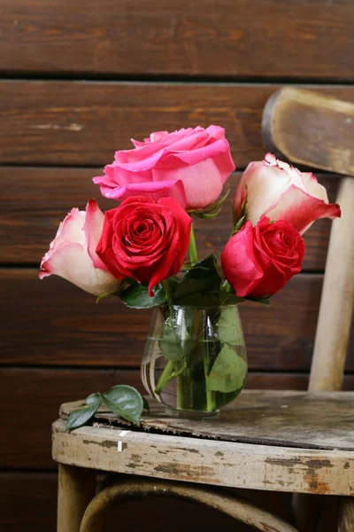 Buquê de rosas em um vaso de vidro em um fundo de madeira — Fotografia de Stock