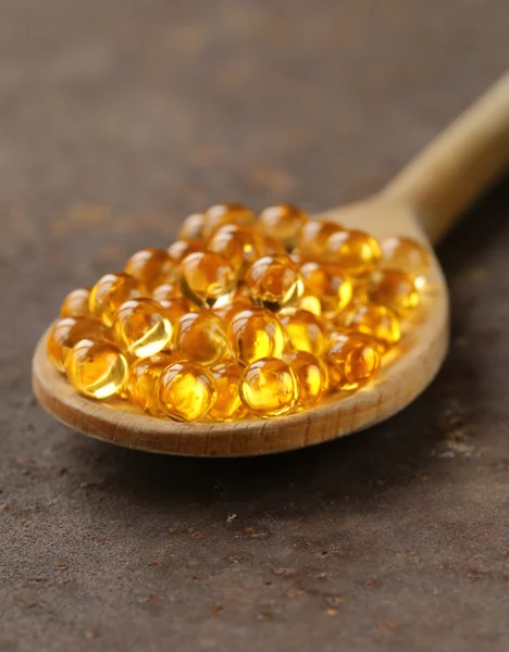 Suplemento alimenticio de cápsulas de aceite de pescado en una cuchara de madera - comida saludable —  Fotos de Stock