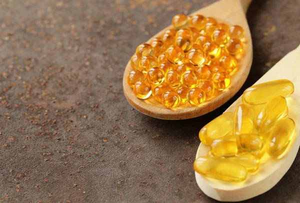 Suplemento alimenticio de cápsulas de aceite de pescado en una cuchara de madera - comida saludable —  Fotos de Stock