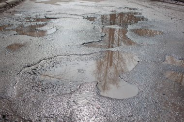 Kötü asfalt yol. Suyla dolu büyük bir çukur. Tehlikeli yol yatağı yok edildi. Sudaki ayna yansıma ağaçları.