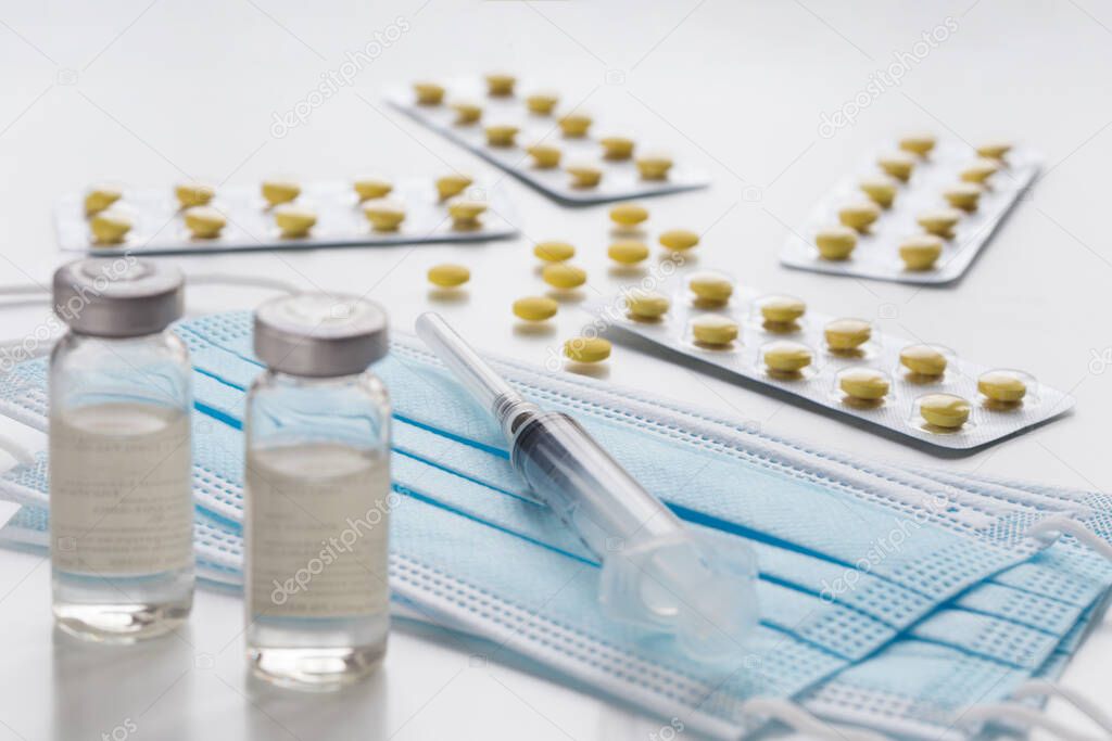 Packagings with yellow pills, medical bottles, expendable syringe for vaccination and protective face mask. Coronavirus vaccination concept.