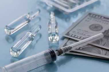 Üç ampulla, aşı için harcanabilir şırınga ve kağıt para. Sigorta hekimliği konsepti, yüksek uyuşturucu maliyeti.