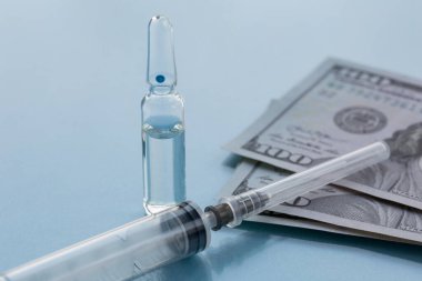 Ampullas, aşı için harcanabilir şırınga ve kağıt para. Sigorta tıbbı kavramı, yüksek maliyetli ilaçlar. Mavi bir arkaplanda izole edilmiş.