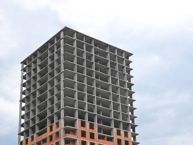 Altında tuğla olan çok katlı beton bir yapı. Arkaplanda ışık bulutlu gökyüzü inşaatı.