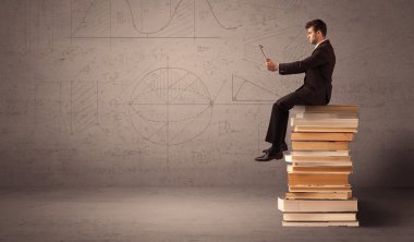 Tabletli bir iş adamı kitapların üzerinde oturuyor.