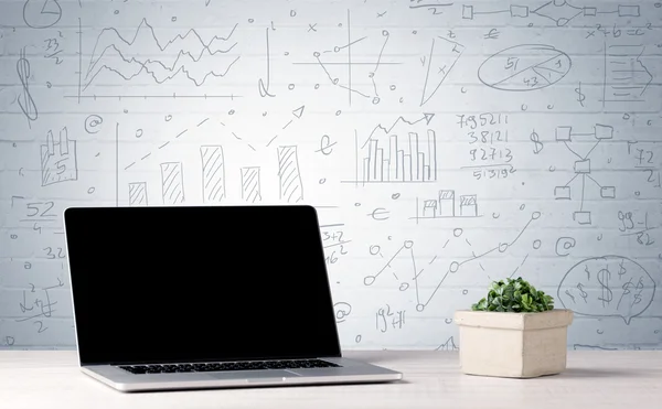 Laptop na mesa com gráficos de negócios na parede — Fotografia de Stock
