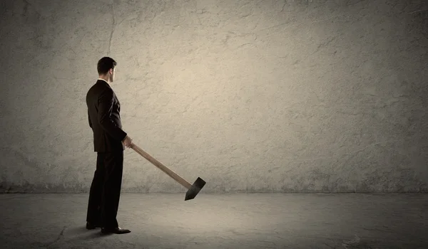 Hombre de negocios de pie frente a una pared grumosa con un martillo — Foto de Stock