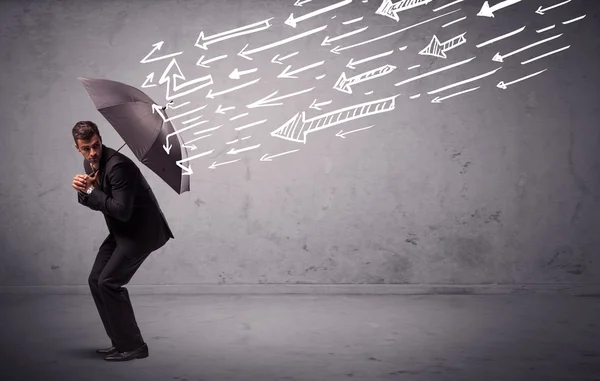 Homem de negócios de pé com guarda-chuva e flechas desenhadas batendo nele — Fotografia de Stock