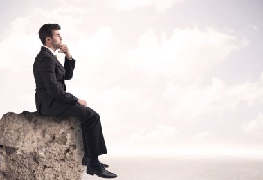 İş adamı taşın üstünde oturuyor.