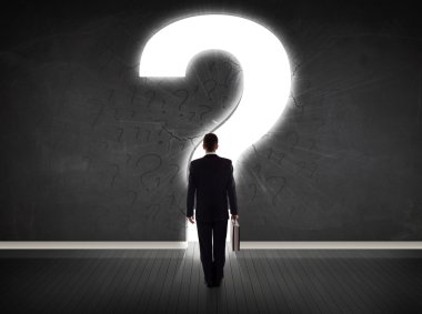 Parlak bir soru işaretiyle duvara bakan bir iş adamı 