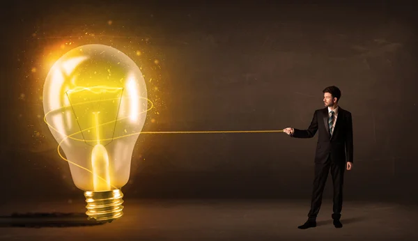 Business man pulling a big bright glowing light bulb — Stock Photo, Image