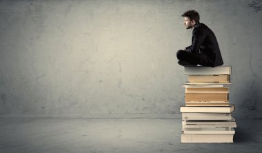 Öğrenci kitap yığınının üzerinde oturuyor