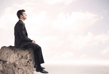 İş adamı taşın üstünde oturuyor.