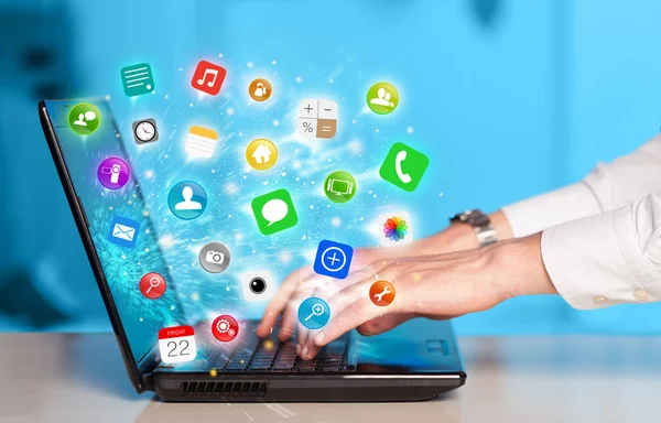Main appuyant sur ordinateur portable moderne avec des icônes d'application mobile et des symboles — Photo