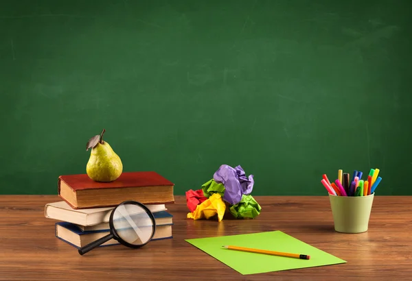 Itens escolares na mesa com quadro-negro vazio — Fotografia de Stock