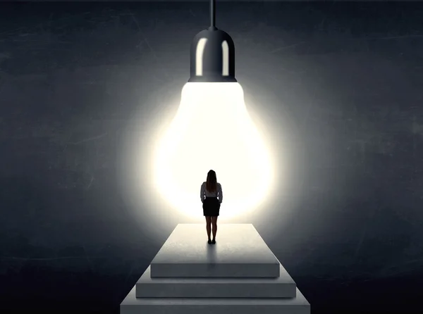 Woman standing on a step in front of a huge light bulb — Stock Photo, Image