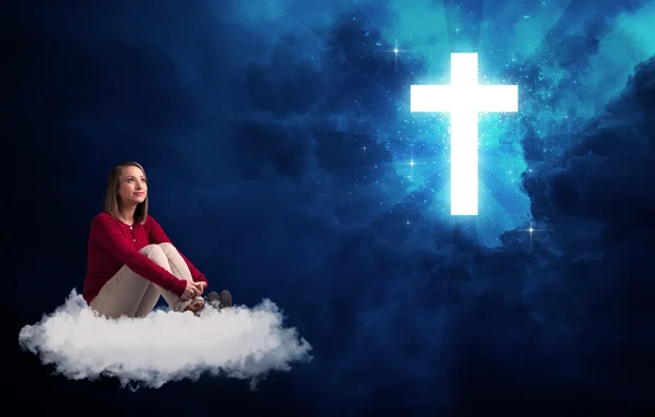 Femme assise sur un nuage regardant une croix — Photo