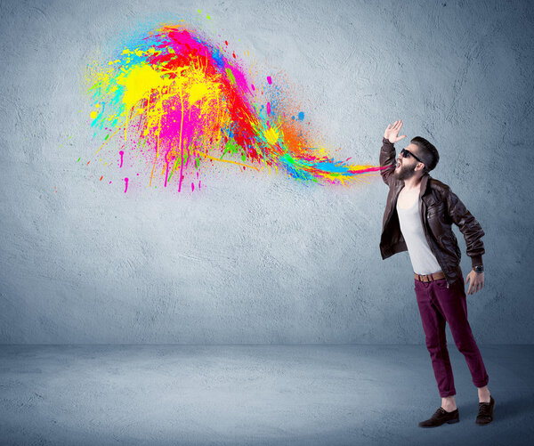 Hipster guy shouting colorful paint on wall