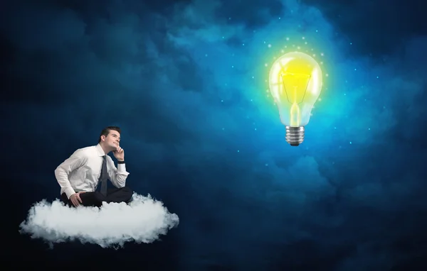 Uomo seduto sulla nuvola a guardare una lampadina — Foto Stock