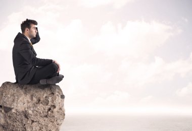 İş adamı taşın üstünde oturuyor.