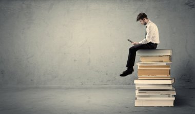 Adam kitaplar üzerinde oturan dizüstü bilgisayar ile