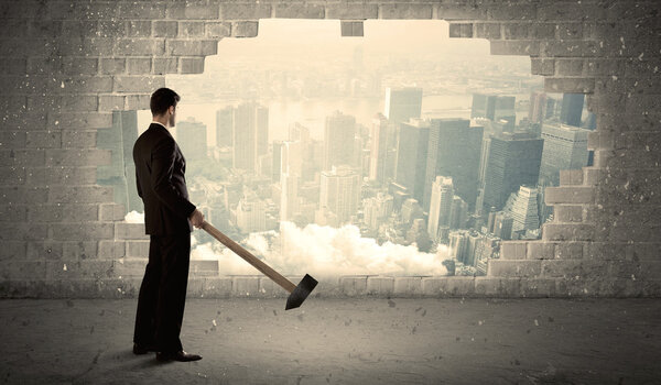 Деловой человек бьет молотком по стене с видом на город