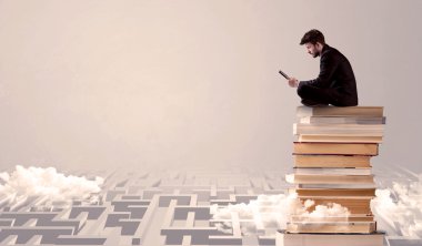 Tabletli adam kitapların üzerinde oturuyor.