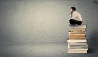 Öğrenci kitap yığınının üzerinde oturuyor