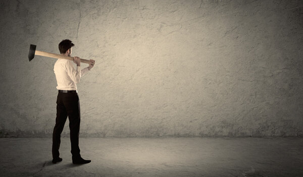Business man standing in front of a grungy wall with a hammer