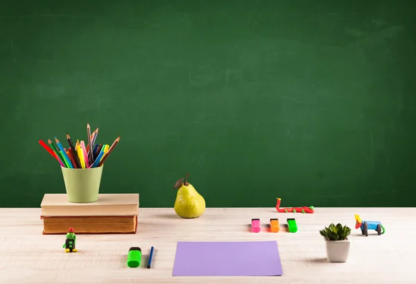 Itens escolares na mesa com quadro-negro vazio — Fotografia de Stock