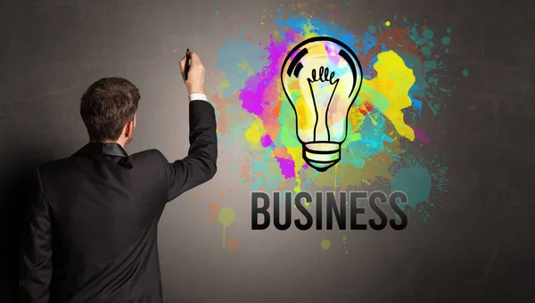 Businessman drawing colorful light bulb — Stock Photo, Image