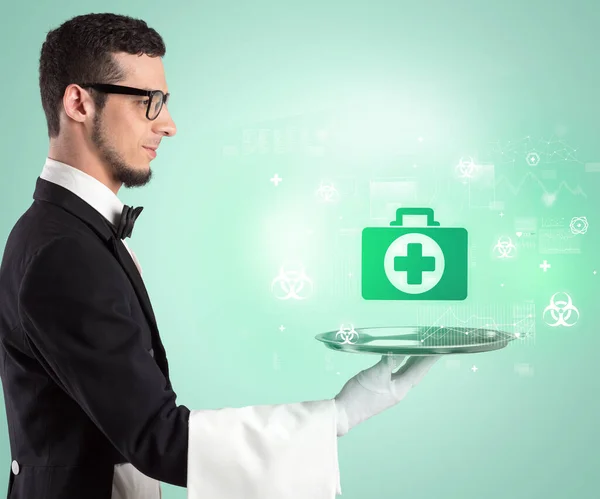 Handsome young waiter in tuxedo holding healthcare icons on tray — Stock Photo, Image