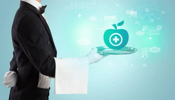 Handsome young waiter in tuxedo holding healthcare icons on tray — Stock Photo, Image