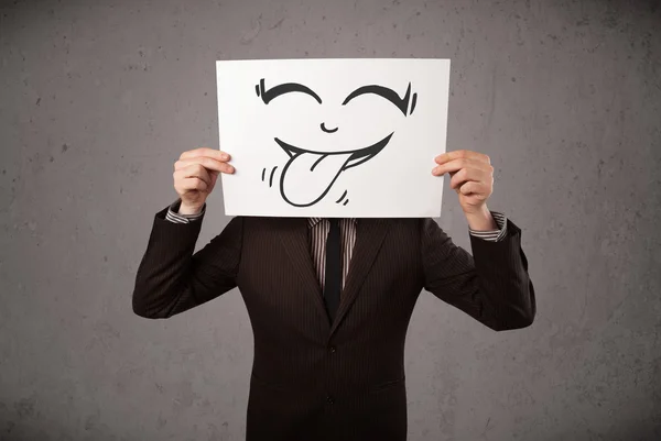 Businessman holding a paper with funny smiley face in front of h — Stock Photo, Image