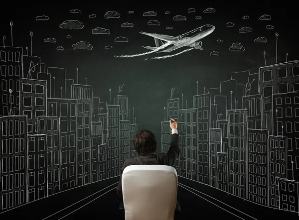 Businessman sitting in front of a cityscape drawing on a chalkbo — Stock Photo, Image